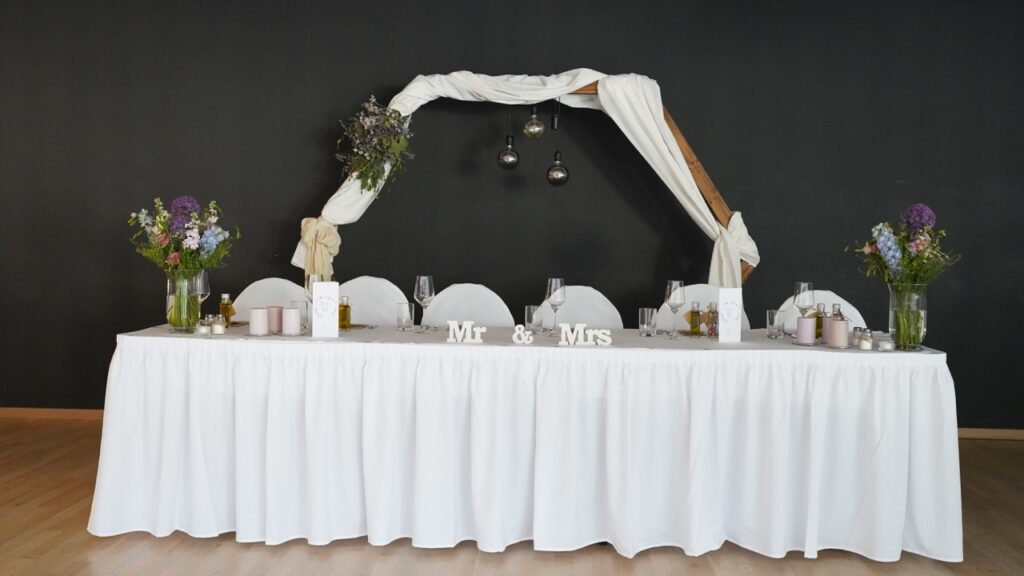 Ein Hochzeitstisch mit einer weißen Tischdecke und Blumen.