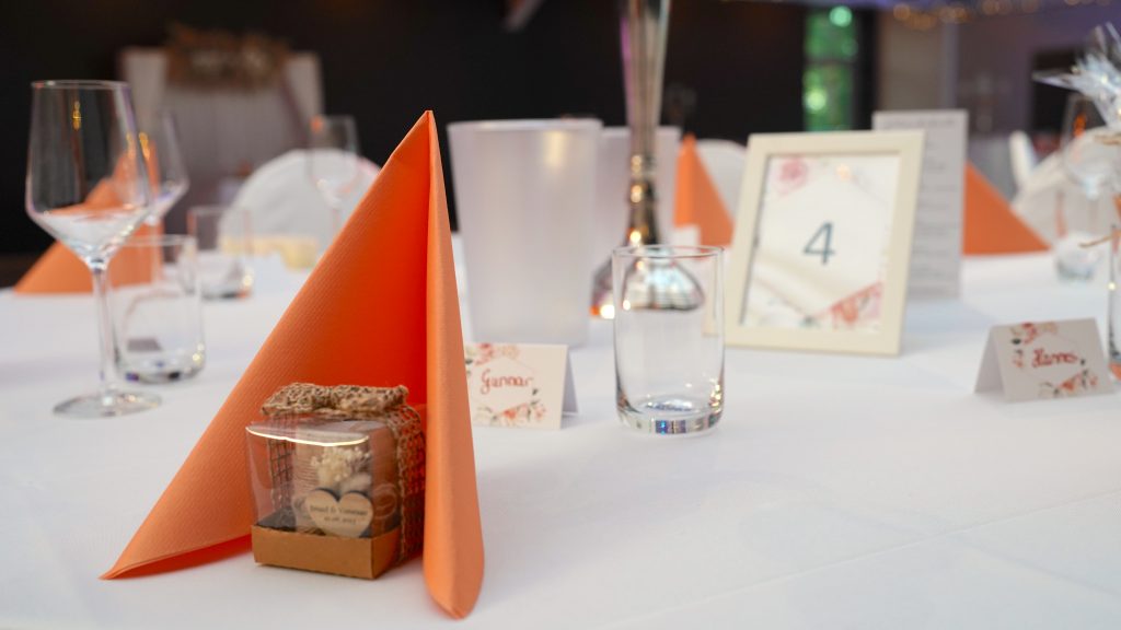 Gedeckter Tisch Mit Orangefarbenen Servietten Und Einem Glasgefäß.